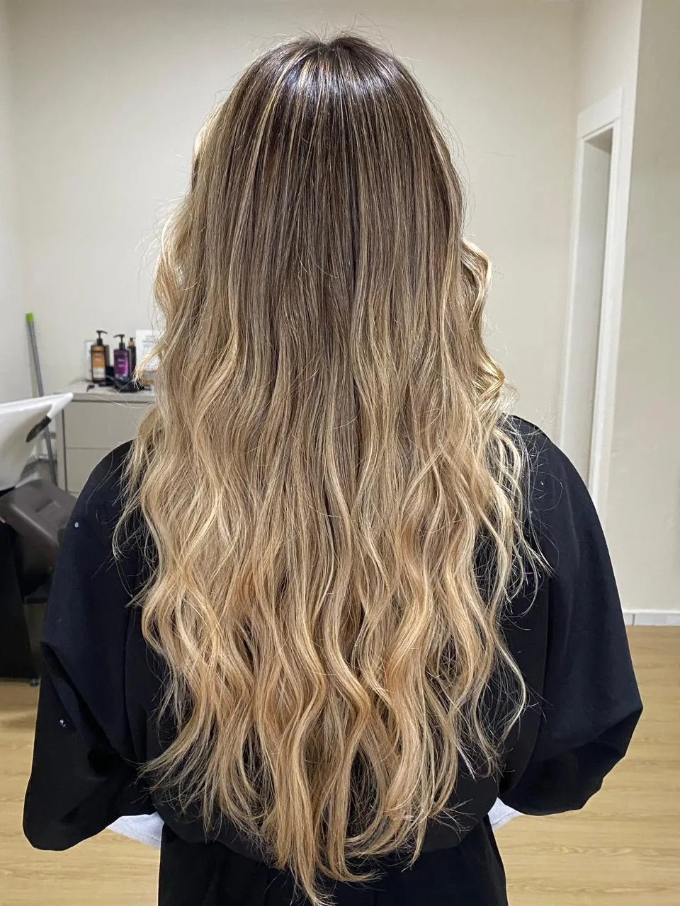 Cliente de costas com cabelo longo ondulado, com tons claros nos comprimentos